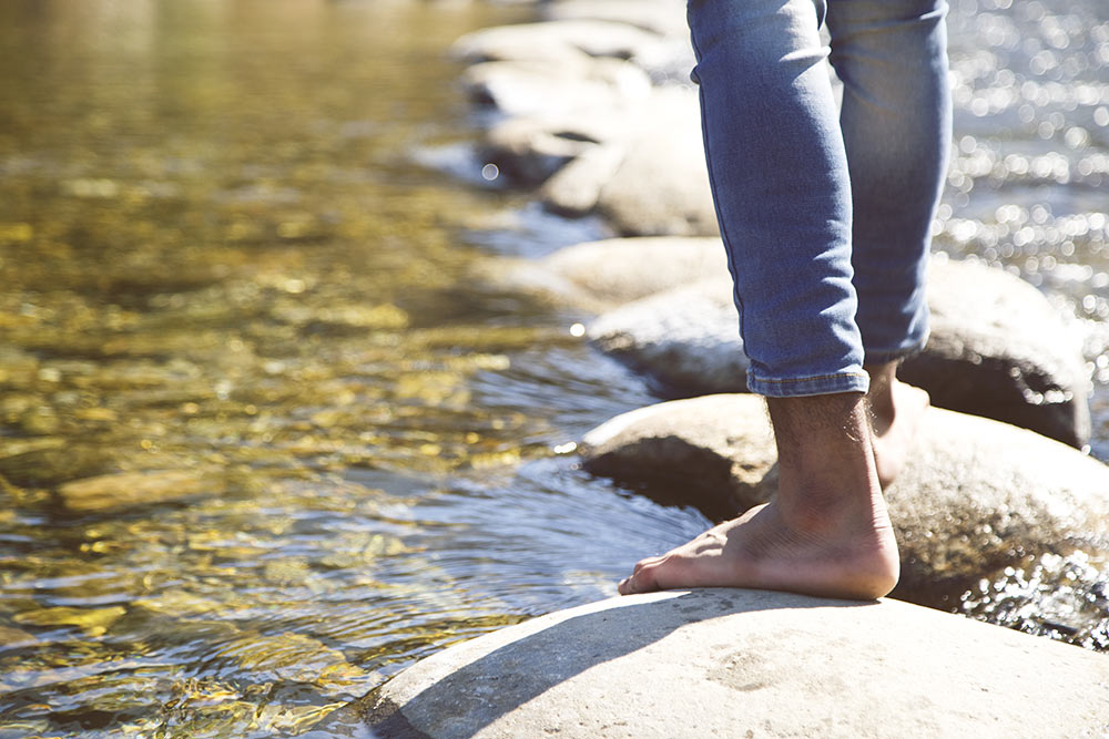 Mit nackten Füßen über Trittsteine in einem Bach